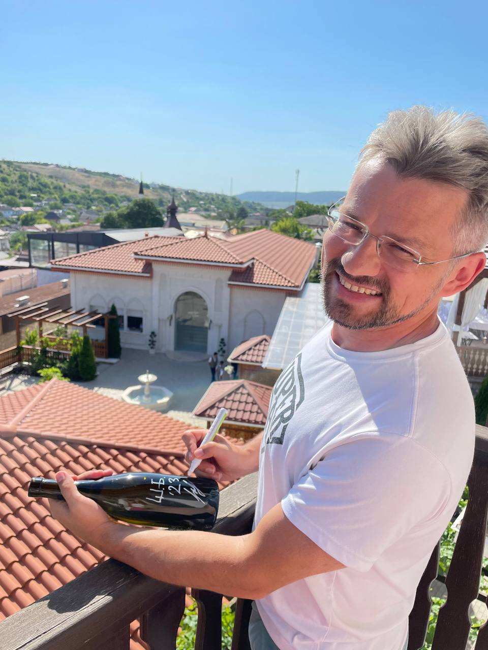 Дмитрий Вишневецкий подписывает бутылку Шенен Блан на фоне виноградника